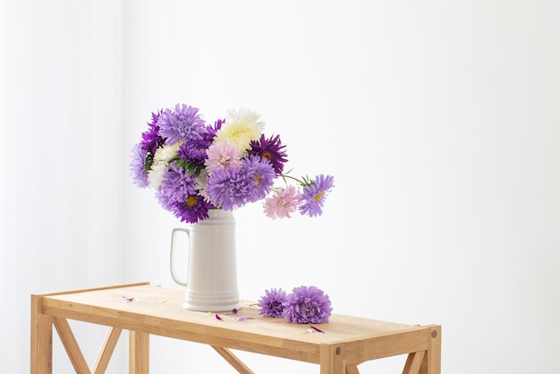 Beautiful bouquet of asters in white jug on background white wall