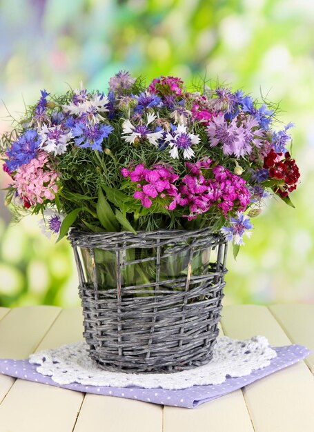 Beautiful bouquet in basket on wooden table on natural background