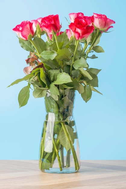 Beautiful bouquet of bright flowers in glass vase on blue background