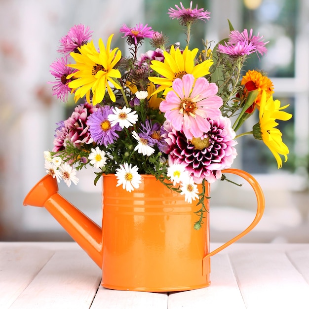 Beautiful bouquet of bright flowers in watering can on wooden table