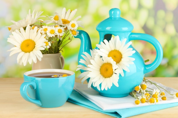 Beautiful bouquet chamomiles in teapot on wooden table on natural background