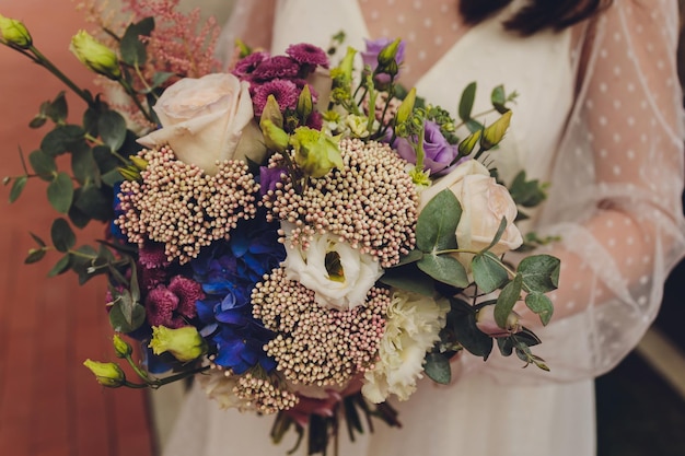 Beautiful bouquet of different colors in the hands of the bride in a white dress