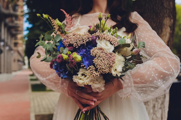 Beautiful bouquet of different colors in the hands of the bride in a white dress