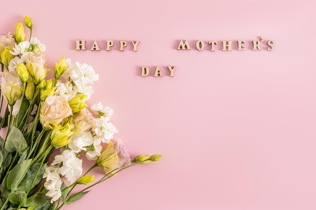 Beautiful bouquet in light colors of spring flowers on pink background with wooden letters and mothers day wish text Holiday concept