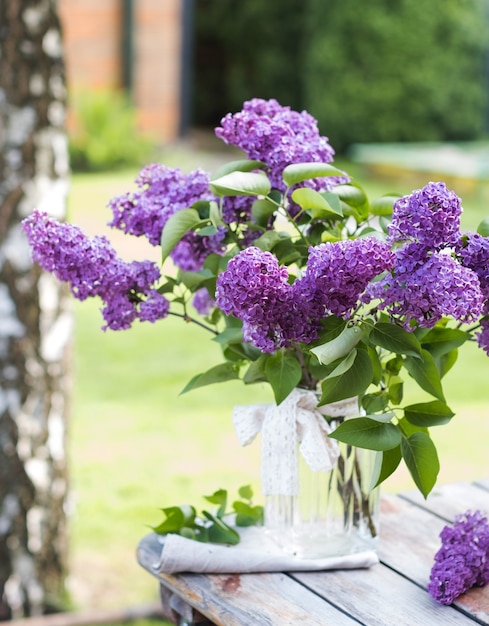 Beautiful bouquet of lilacs in a vase on wooden table in nature