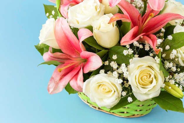 Beautiful bouquet of pink lilies and white roses in a wicker basket on a blue background