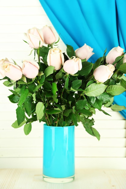 Beautiful bouquet of roses in vase, on light wooden background