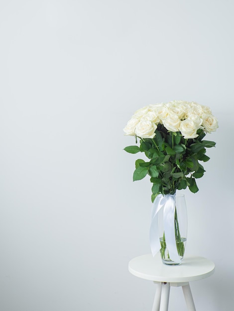 Beautiful bouquet of white blooming roses in glass vase on round table