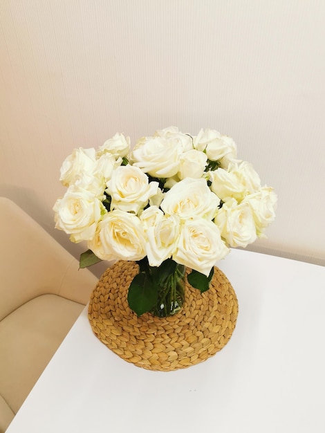 A beautiful bouquet of white roses in a glass vase on a white table and interior on a wicker