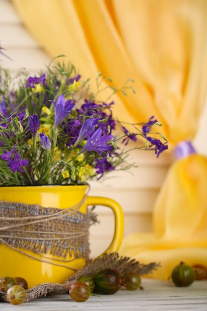 Beautiful bouquet of wildflowers in cup and berries on wooden table