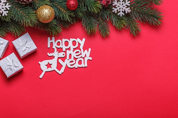 Beautiful branches of a Christmas tree with cones and toys on a red background with the inscription Happy New Year