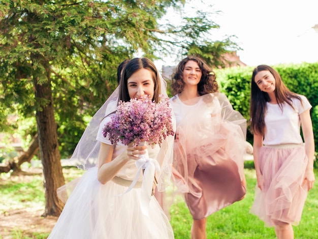 The beautiful bride covers her face with a bouquet of lilac and the girlfriends behind her