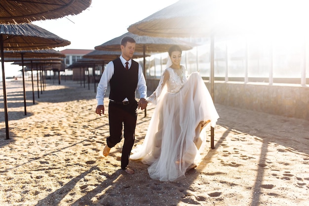 Photo beautiful bride and groom stroll along sandy beach holding hands happy wedding couple on sea beach