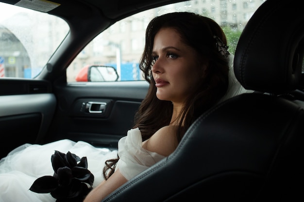 The beautiful bride is sitting in a red car in a white dress and with a bouquet. Wedding Concept