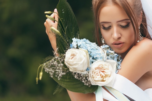 Photo beautiful bride in a magnificent wedding dress posing among greenery on the street. girl poses in a wedding dress for advertising. bride concept for advertising dresses.