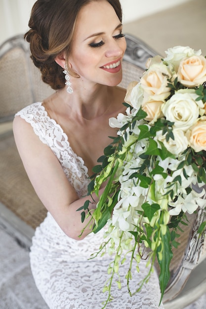 Beautiful bride posing in wedding dress in a white photo Studio. Mirror. Sofa. Bouquet. The door. Chandelier.