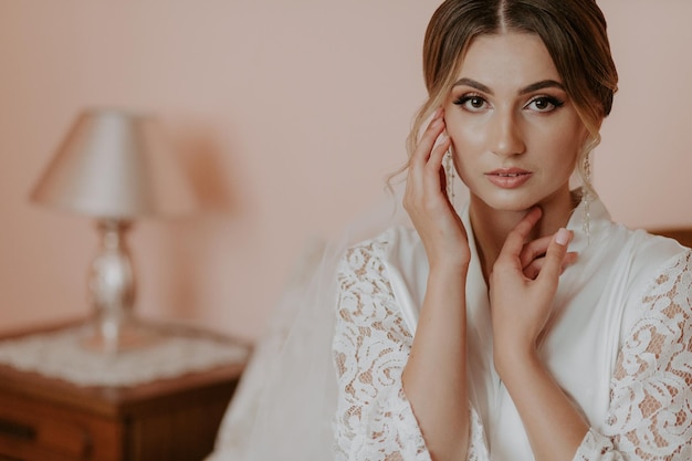 Beautiful bride in robe posing near window, wedding preparation