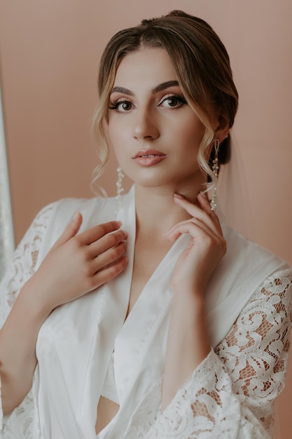 Beautiful bride in robe posing near window, wedding preparation