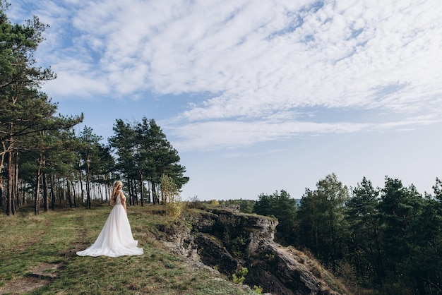 a beautiful bride in a white dress stands on top of a mountain