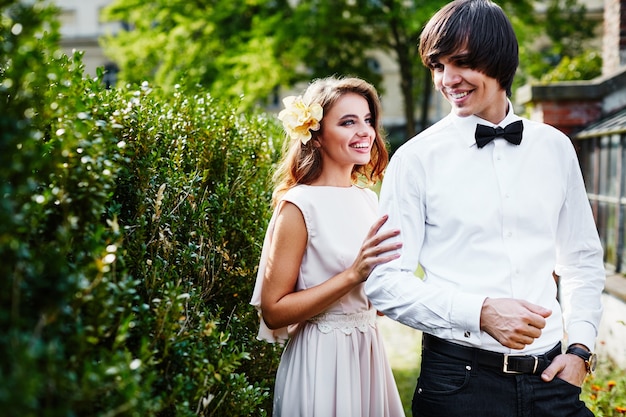 Beautiful bride with long curly hair and bridegroom standing close to each other at green leaves background, wedding photo, wedding day, portrait.