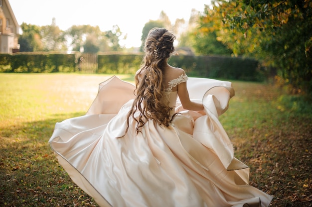 Beautiful bride with a long hair in a white dress running in the green park. Conception of the wedding