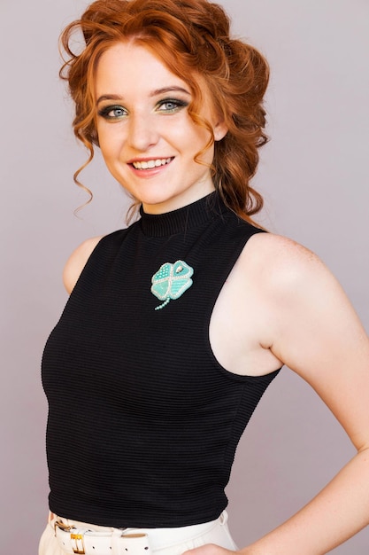 Beautiful brooch in the form of a clover on a black sleeveless jacket of a stylish redhaired girl