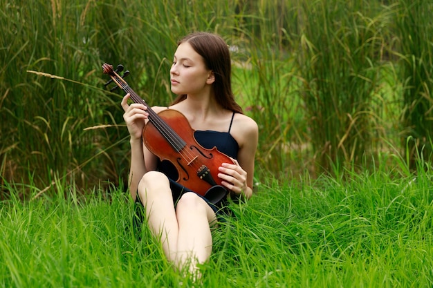 Beautiful brown-haired girl of Asian appearance with a violin in nature. musician in nature. classical music. High quality photo