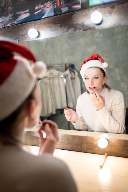 Beautiful brown-haired woman in white sweater looks in the makeup mirror