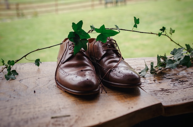 Beautiful brown stylish groom shoes on a wooden table with ivy branch