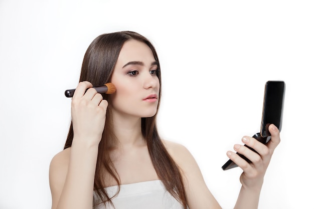 Beautiful brunette applies cosmetic powder on her face with a brush