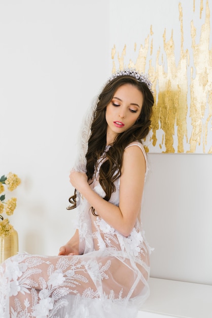 beautiful brunette bride with long hair with a tiara in a negligee holding a white ostrich feather.