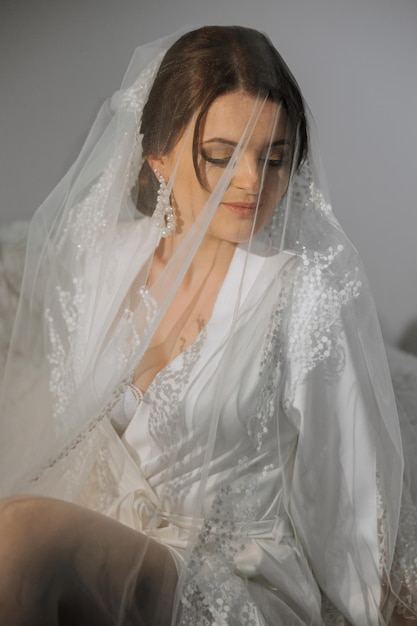 A beautiful brunette bride with a tiara in her hair is getting ready for the wedding in a beautiful robe in boudoir style Closeup wedding portrait photo