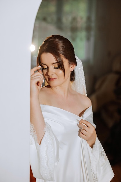 A beautiful brunette bride with a tiara in her hair is getting ready for the wedding in a beautiful robe in boudoir style Closeup wedding portrait photo