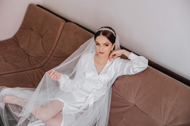 A beautiful brunette bride with a tiara in her hair is getting ready for the wedding in a beautiful robe in boudoir style Closeup wedding portrait photo