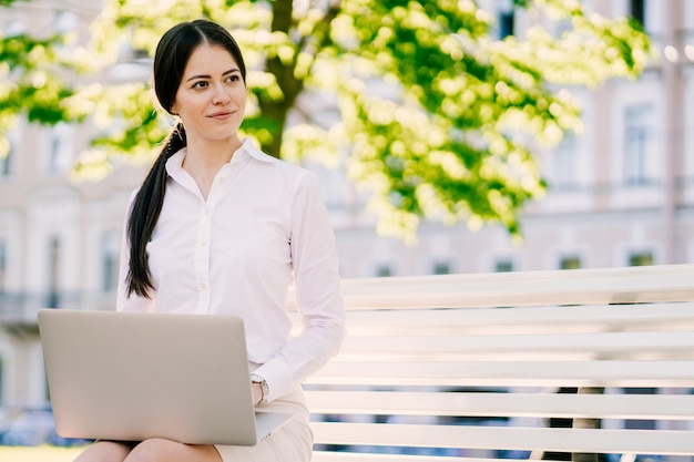 Beautiful brunette businesswoman in white shirt, remote working outdoor on her laptop outdoor,