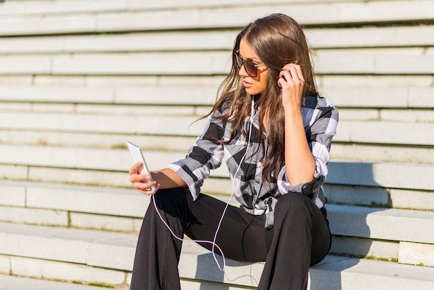 Beautiful brunette caucasian girl listening to the music with headphones on stairs in the city