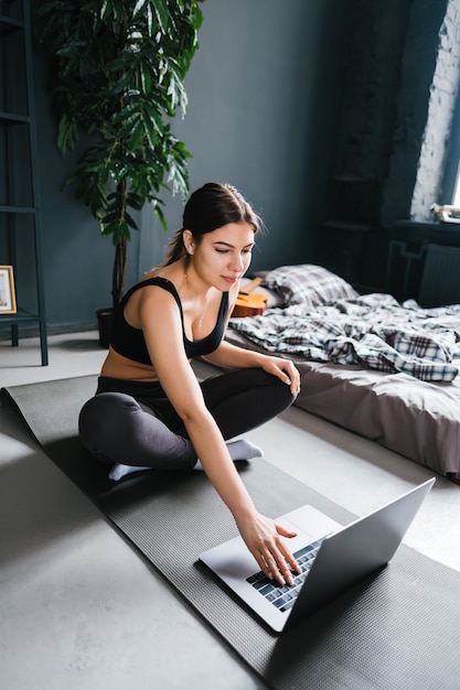 Beautiful brunette fitness woman make stretching exercises in front laptop, doing yoga indoors at home