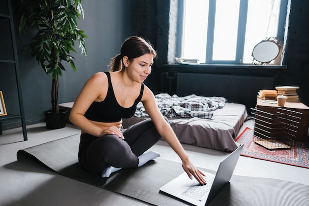 Beautiful brunette fitness woman make stretching exercises in front laptop, doing yoga indoors at home