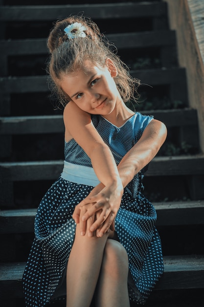 Beautiful brunette girl in a blue polka dot dress on the steps of the stairs in the park. High quality photo