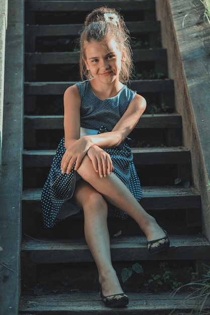 Beautiful brunette girl in a blue polka dot dress on the steps of the stairs in the park. High quality photo