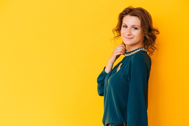 A beautiful brunette girl in a green blouse with a golden brooch in the form of the moon poses against a yellow background The girl looks at the camera and smiles