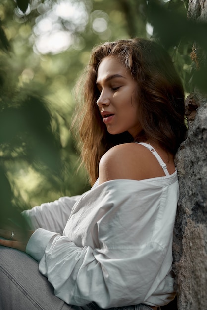 beautiful brunette girl in jeans and a white shirt posing on the ruins in the forest