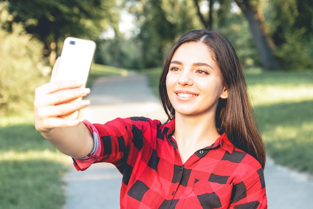 beautiful brunette girl in a red plaid shirt taking selfie