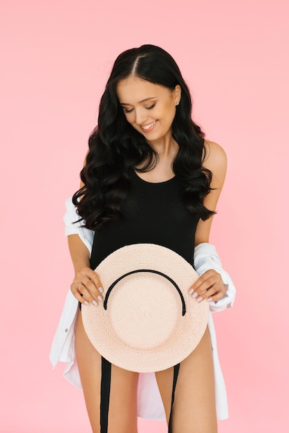 Beautiful brunette holds a hat in her hands on a pink background