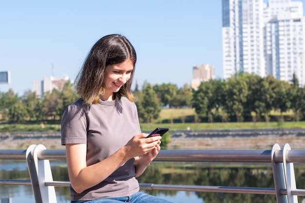 A beautiful brunette student with glasses uses a smartphone on the street A beautiful student girl uses the phone