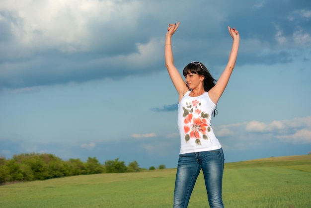 A beautiful brunette with big breasts stands against the blue sky in a white Tshirt