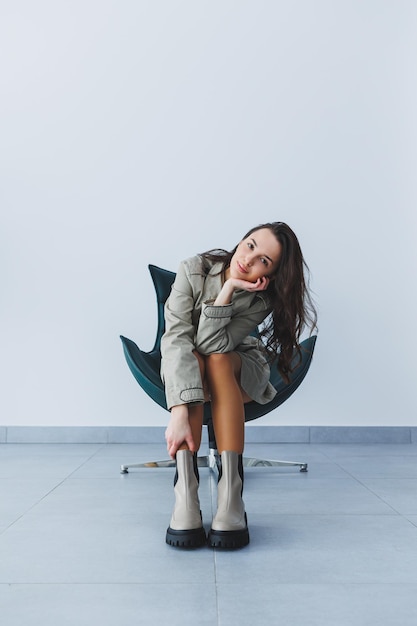 Beautiful brunette woman in an autumn trench coat and leather boots posing in the studio Women's fashion