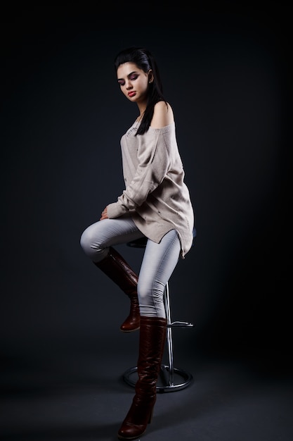 Beautiful brunette woman in beige sweater sitting on a bar stool