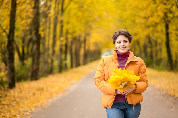 Beautiful brunette woman posing in a yellow jacket in an autumn park with a bouquet of autumn leaves