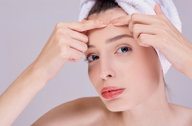 A beautiful brunette woman presses a pimple on her forehead.